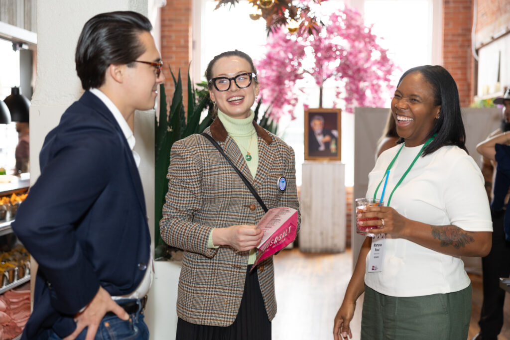 Three people at the Elevate reception are chatting about place-based learning and evaluation. 